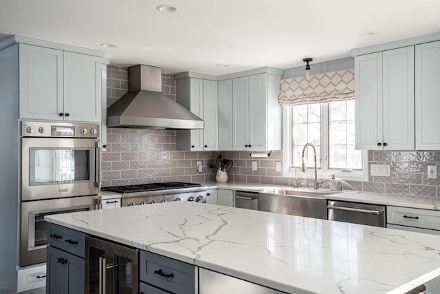 kitchen featuring wine cooler, appliances with stainless steel finishes, wall chimney exhaust hood, and light stone counters