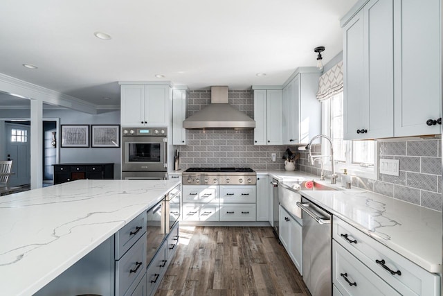 kitchen featuring appliances with stainless steel finishes, pendant lighting, wall chimney range hood, and light stone counters