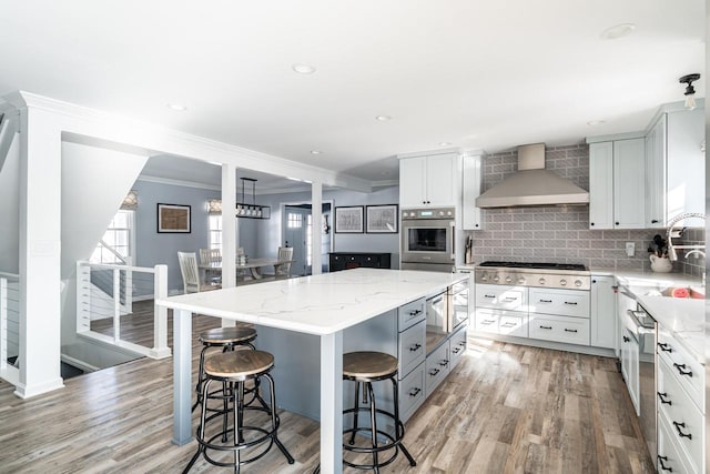 kitchen with stainless steel appliances, light stone counters, wall chimney range hood, a kitchen island, and a kitchen bar