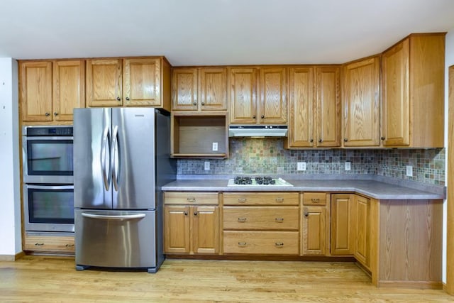 kitchen featuring under cabinet range hood, light wood-style flooring, stainless steel appliances, and tasteful backsplash