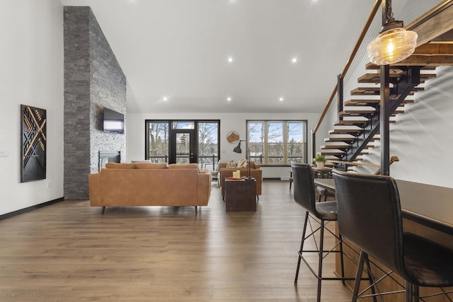 living room featuring a stone fireplace, wood-type flooring, and high vaulted ceiling