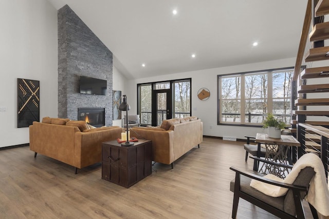 living room featuring high vaulted ceiling, a fireplace, and light hardwood / wood-style floors