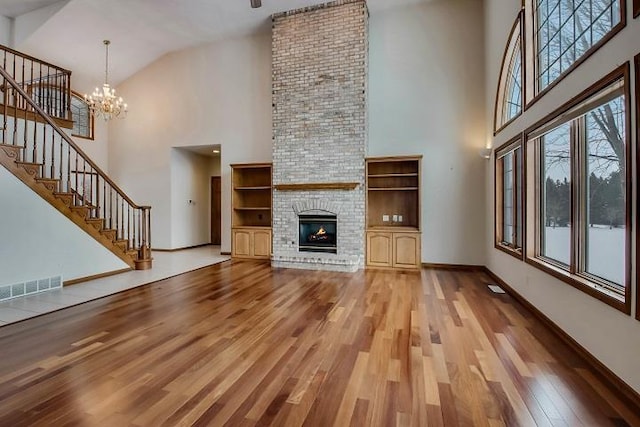 unfurnished living room with a brick fireplace, high vaulted ceiling, an inviting chandelier, and light hardwood / wood-style flooring