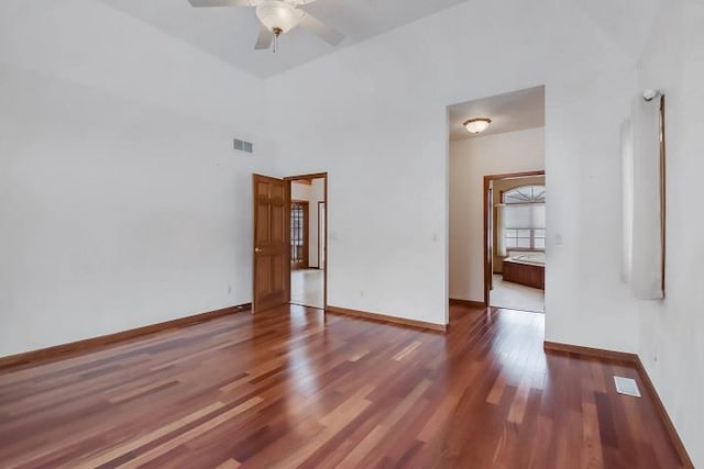 empty room featuring dark wood-type flooring, ceiling fan, and a high ceiling