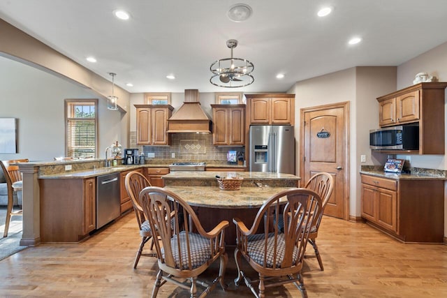 6507 Willow Ct, Waterford, WI 53185 - kitchen with wall chimney exhaust hood, a kitchen bar, hanging light fixtures, appliances with stainless steel finishes, and kitchen peninsula
