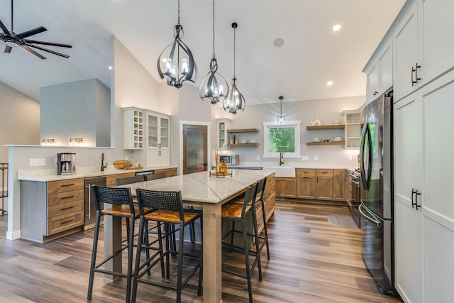 kitchen with a spacious island, glass insert cabinets, freestanding refrigerator, light stone countertops, and open shelves