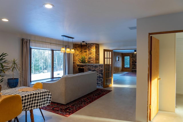 living room with an inviting chandelier, a brick fireplace, and concrete floors