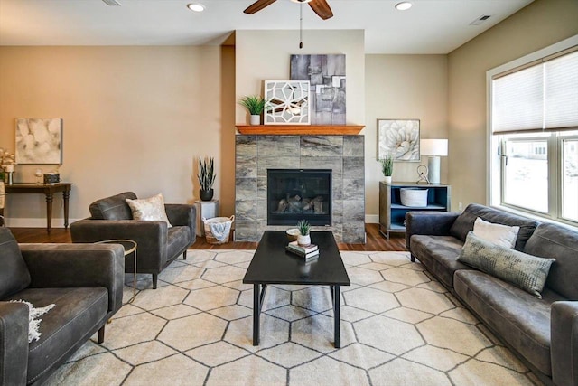 living room with a tile fireplace, ceiling fan, and light wood-type flooring