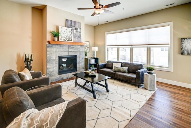 living room with ceiling fan, a tile fireplace, and light wood-type flooring