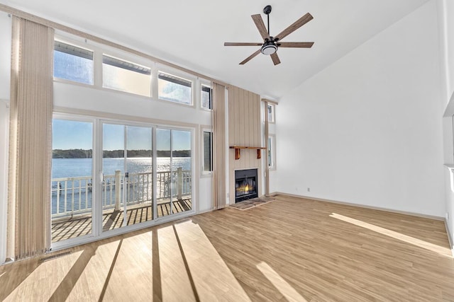 unfurnished living room featuring ceiling fan, high vaulted ceiling, a water view, a fireplace, and light hardwood / wood-style floors