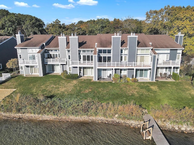 back of house featuring a balcony, a water view, and a lawn