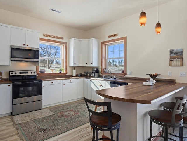 kitchen with appliances with stainless steel finishes, white cabinets, a kitchen breakfast bar, and kitchen peninsula