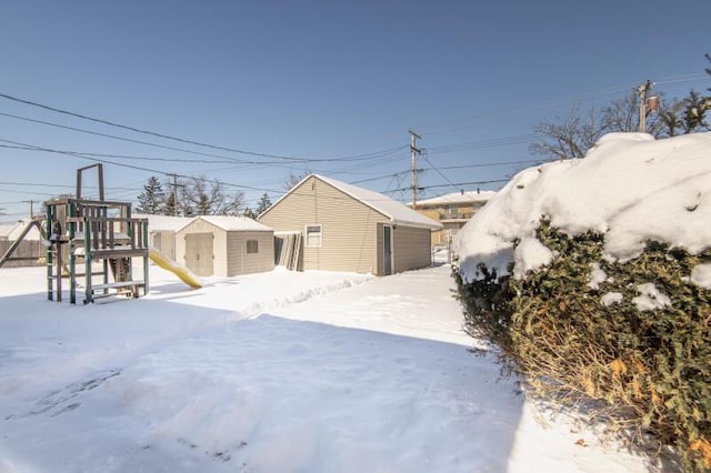 snowy yard featuring a playground and a storage unit