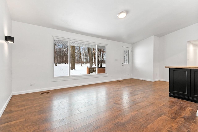 unfurnished living room with baseboards, visible vents, and dark wood-type flooring