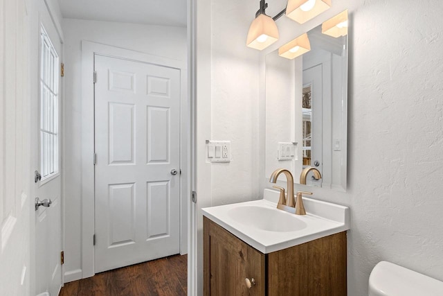 bathroom with toilet, a textured wall, wood finished floors, and vanity