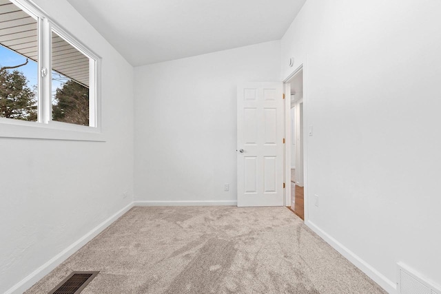 empty room featuring baseboards, visible vents, and light colored carpet