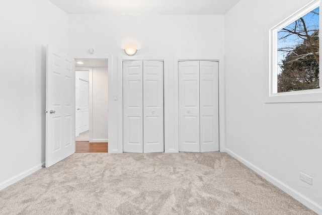 unfurnished bedroom featuring baseboards, multiple closets, and light colored carpet