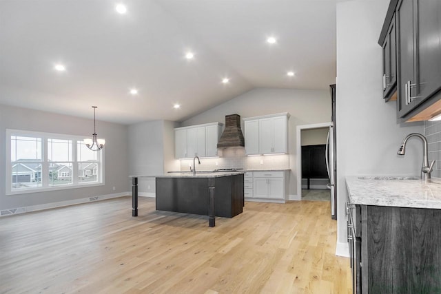 kitchen featuring sink, decorative backsplash, custom exhaust hood, light stone counters, and light hardwood / wood-style floors