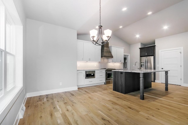 kitchen with white cabinetry, stainless steel appliances, custom range hood, an island with sink, and a kitchen bar