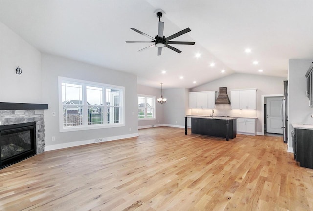 unfurnished living room featuring lofted ceiling, sink, ceiling fan with notable chandelier, a stone fireplace, and light wood-type flooring