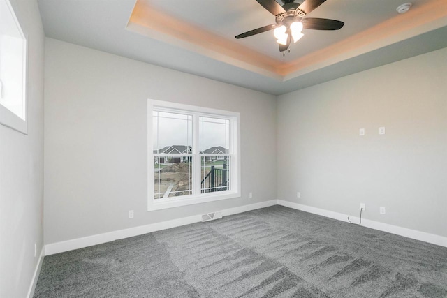 carpeted spare room with a raised ceiling and ceiling fan