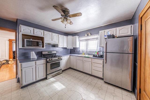 kitchen with dark countertops, stainless steel appliances, under cabinet range hood, white cabinetry, and a sink