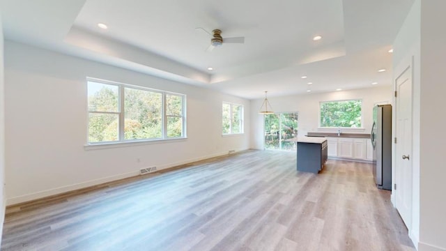 kitchen with pendant lighting, stainless steel refrigerator, white cabinets, a center island, and a raised ceiling