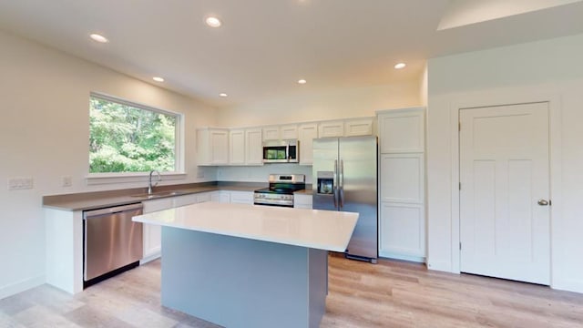 kitchen with sink, stainless steel appliances, a center island, white cabinets, and light wood-type flooring