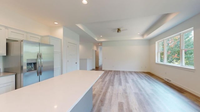 kitchen with stainless steel refrigerator with ice dispenser, white cabinetry, light wood-type flooring, a raised ceiling, and ceiling fan