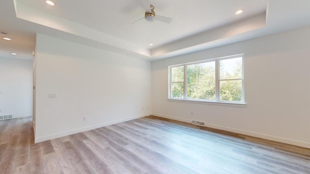 unfurnished room with a tray ceiling, light hardwood / wood-style flooring, and ceiling fan