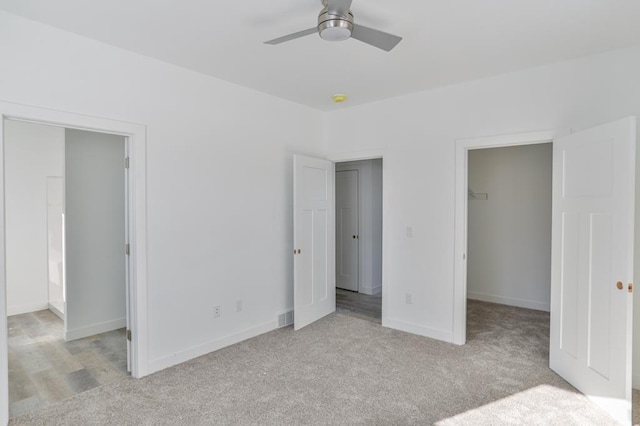 unfurnished bedroom featuring ceiling fan, a walk in closet, light colored carpet, and a closet