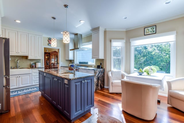 kitchen featuring exhaust hood, hanging light fixtures, appliances with stainless steel finishes, an island with sink, and white cabinets