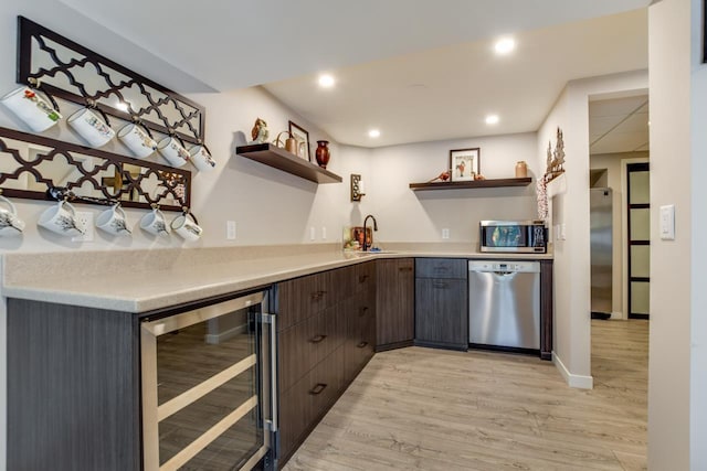 bar with sink, light hardwood / wood-style flooring, appliances with stainless steel finishes, wine cooler, and dark brown cabinetry