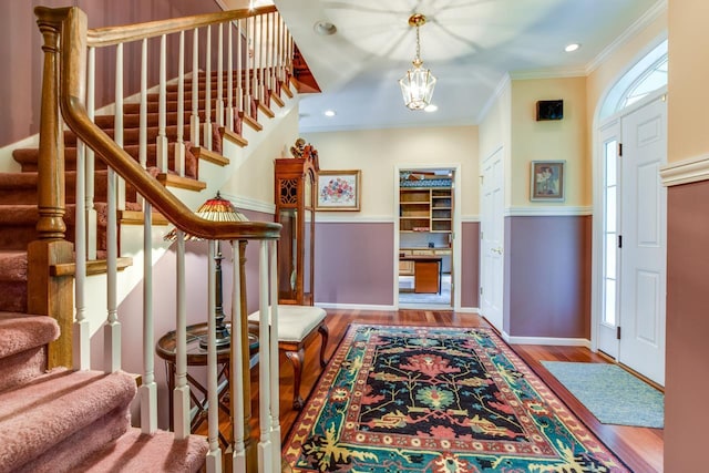 foyer with crown molding, wood-type flooring, and an inviting chandelier