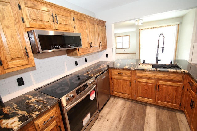 kitchen with sink, appliances with stainless steel finishes, dark stone countertops, tasteful backsplash, and light hardwood / wood-style floors