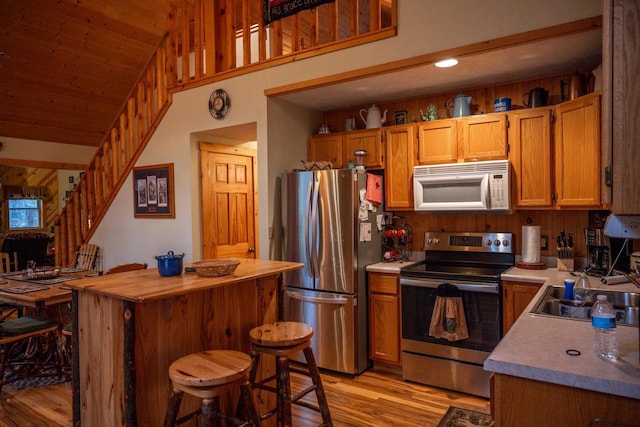 kitchen featuring vaulted ceiling, appliances with stainless steel finishes, sink, a breakfast bar area, and light hardwood / wood-style flooring