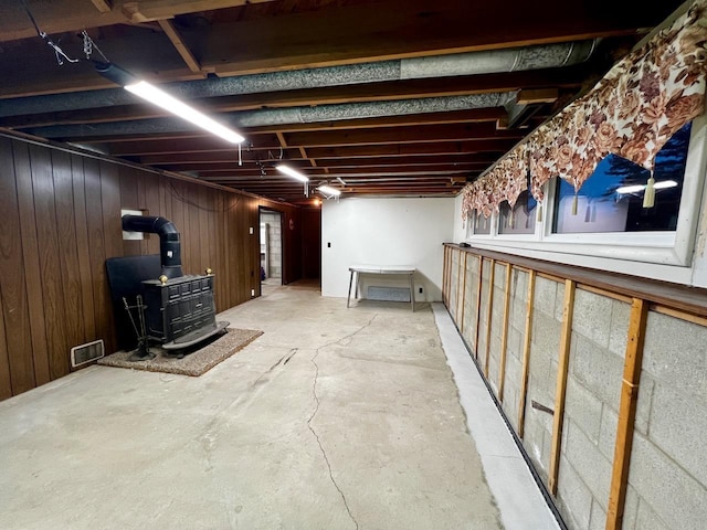 unfinished basement with visible vents, wood walls, and a wood stove