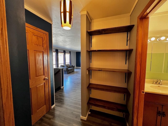 hallway with a textured ceiling, dark wood finished floors, baseboards, and a sink