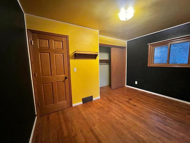 unfurnished bedroom with a closet, visible vents, baseboards, and wood finished floors