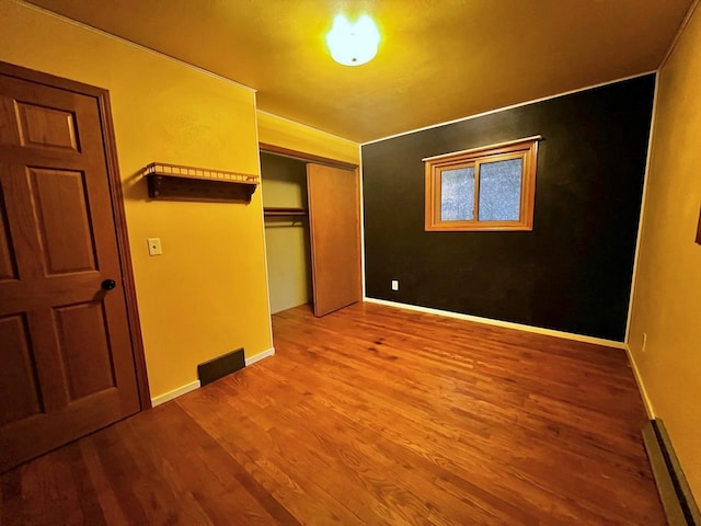 unfurnished bedroom featuring a closet, wood finished floors, baseboards, and a baseboard radiator