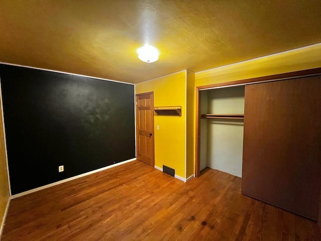 unfurnished bedroom with a closet, baseboards, visible vents, and wood finished floors