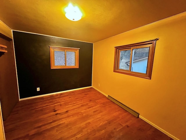 empty room featuring wood finished floors, baseboards, and a baseboard radiator