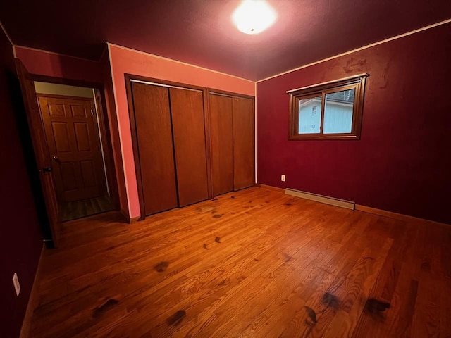 unfurnished bedroom with baseboards, light wood-style floors, multiple closets, and a baseboard radiator