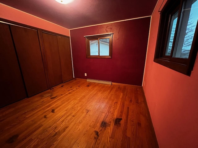 unfurnished bedroom with a baseboard radiator, multiple closets, multiple windows, and wood finished floors