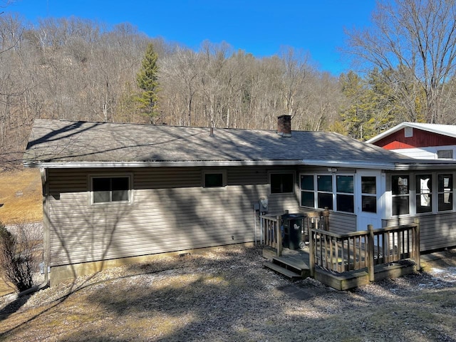 back of house with a chimney, a deck, and roof with shingles