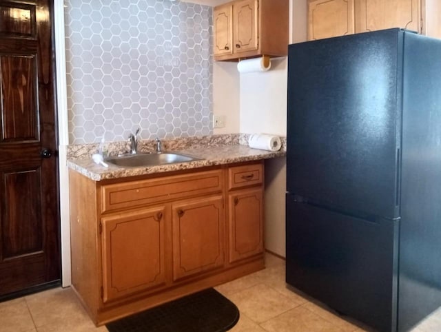 kitchen with light countertops, light tile patterned floors, freestanding refrigerator, and a sink