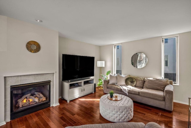 living area with dark wood-style floors, a tiled fireplace, and baseboards