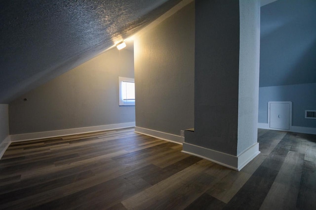 additional living space featuring dark hardwood / wood-style floors, vaulted ceiling, and a textured ceiling