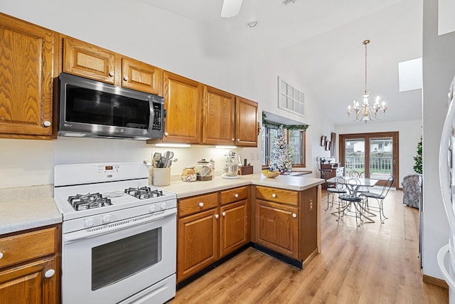 kitchen featuring gas range gas stove, decorative light fixtures, high vaulted ceiling, light wood-type flooring, and kitchen peninsula