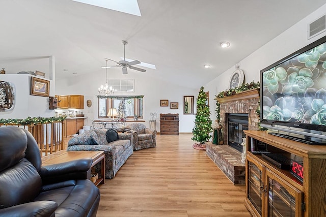 living room with lofted ceiling with skylight, ceiling fan with notable chandelier, a fireplace, and light hardwood / wood-style flooring